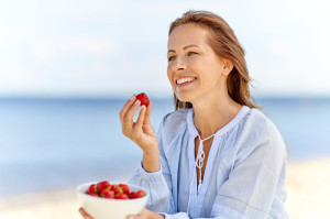 happy woman eating strawberries on summer beach