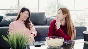 Asian women using smartphone and eating popcorn in living room a